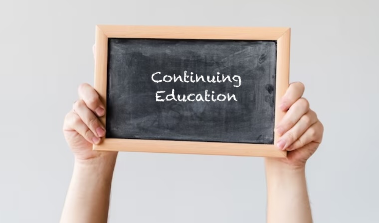 Hand holding a small blackboard with the text 'continuing education'
